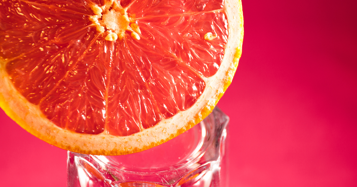 En halv grapefrukt som balanserar p&aring; kanten av ett glas
